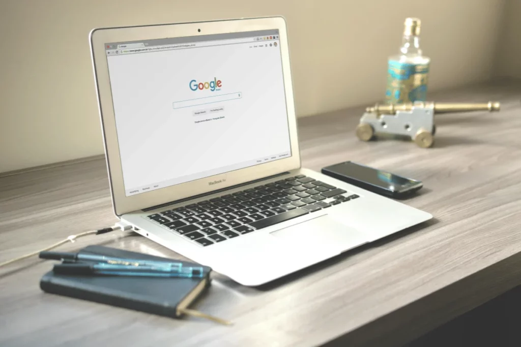Open MacBook Air with Google search screen, next to a notebook and pen.