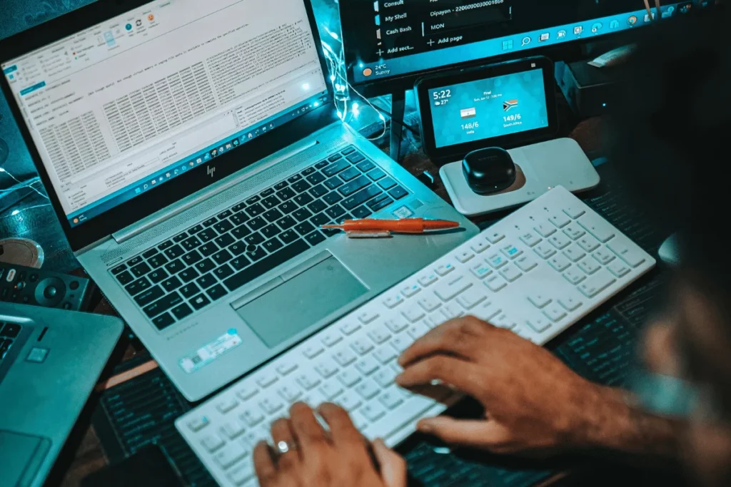 Developer working at a dual-screen setup with a laptop and external keyboard at night.