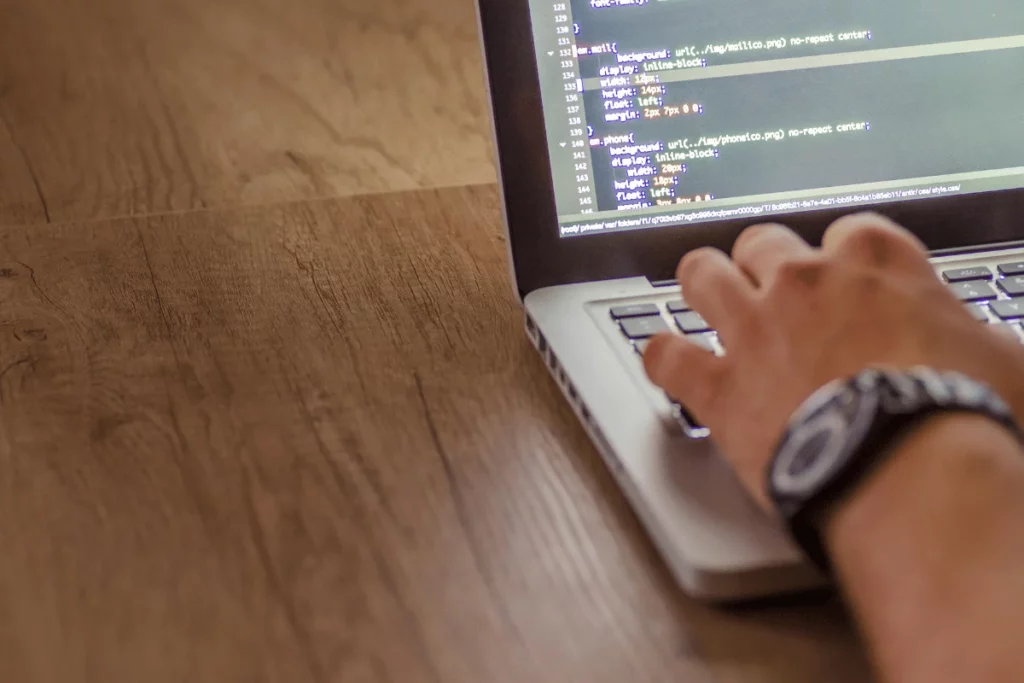 Close-up of a person typing code on a laptop with a CSS stylesheet visible on the screen.