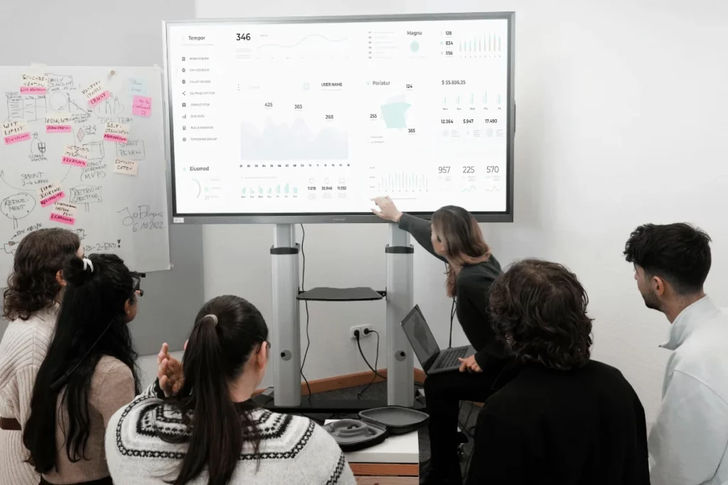 Businesswoman explaining analytics and metrics on a digital display to a group.