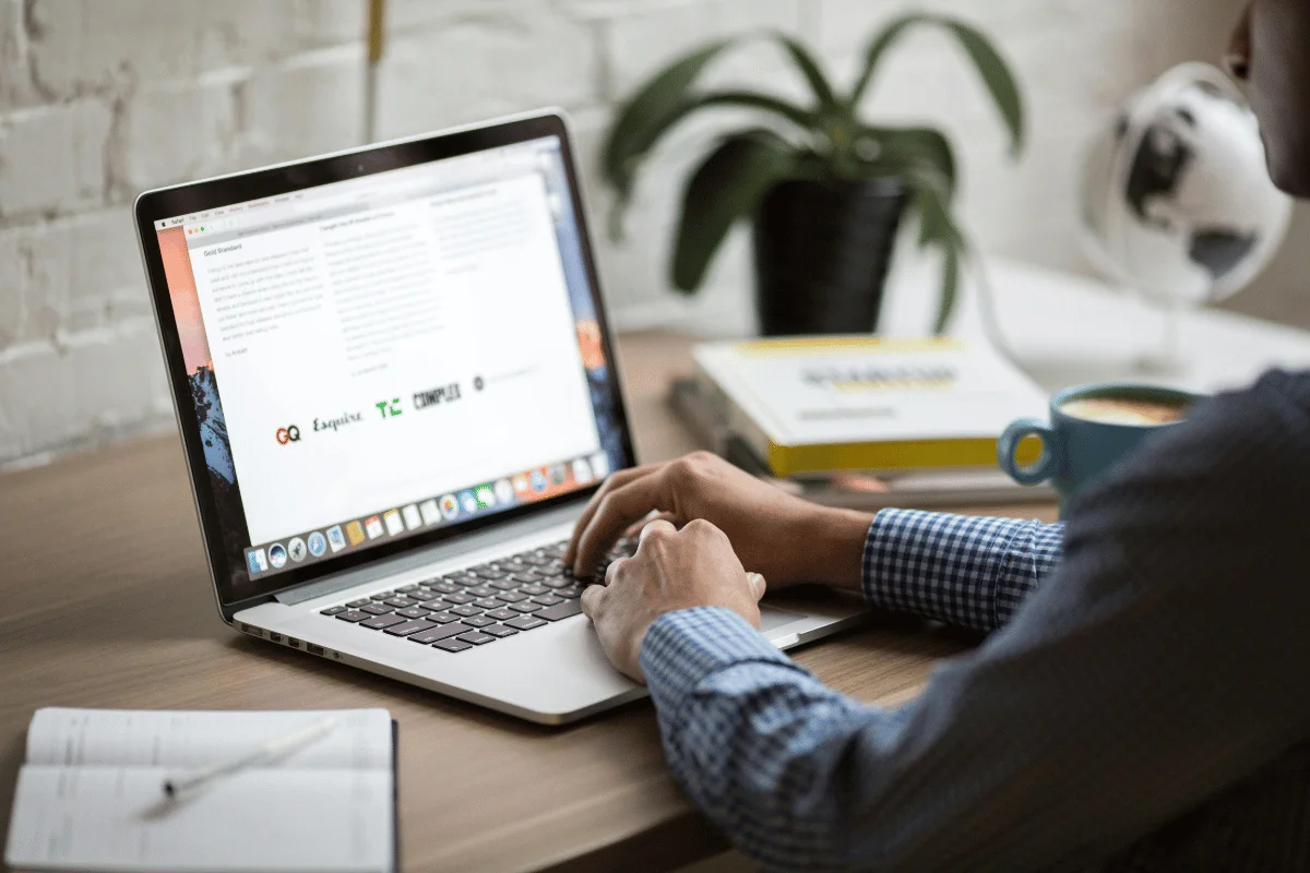 Man typing on a laptop with a minimalist desk setup including books and greenery.