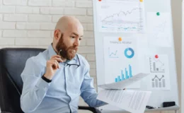 Man analyzing printed reports in front of a finance chart board.