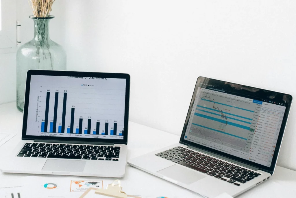 Bar graph on a laptop with financial data, and a second laptop displaying stock market trends.