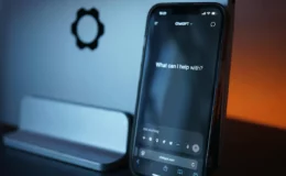 A smartphone displaying the ChatGPT interface, showing the prompt "What can I help with?" on a dimly lit desk.